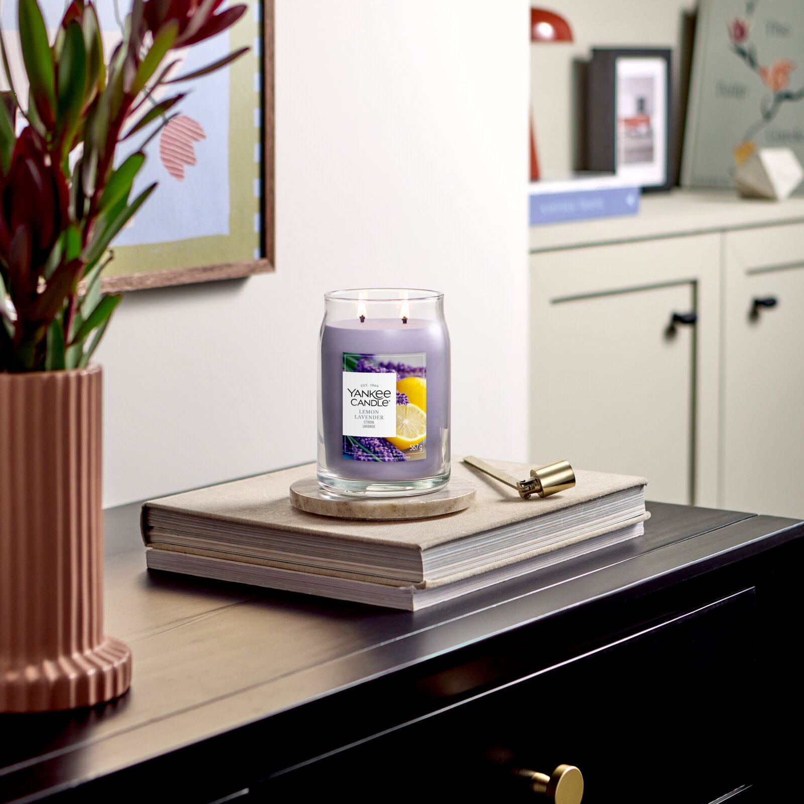 Frontalansicht einer brennenden Yankee Candle Lemon Lavender Duftkerze mit zwei Dochten im großen Glas, dekorativ auf Büchern in einem stilvollen Wohnambiente platziert