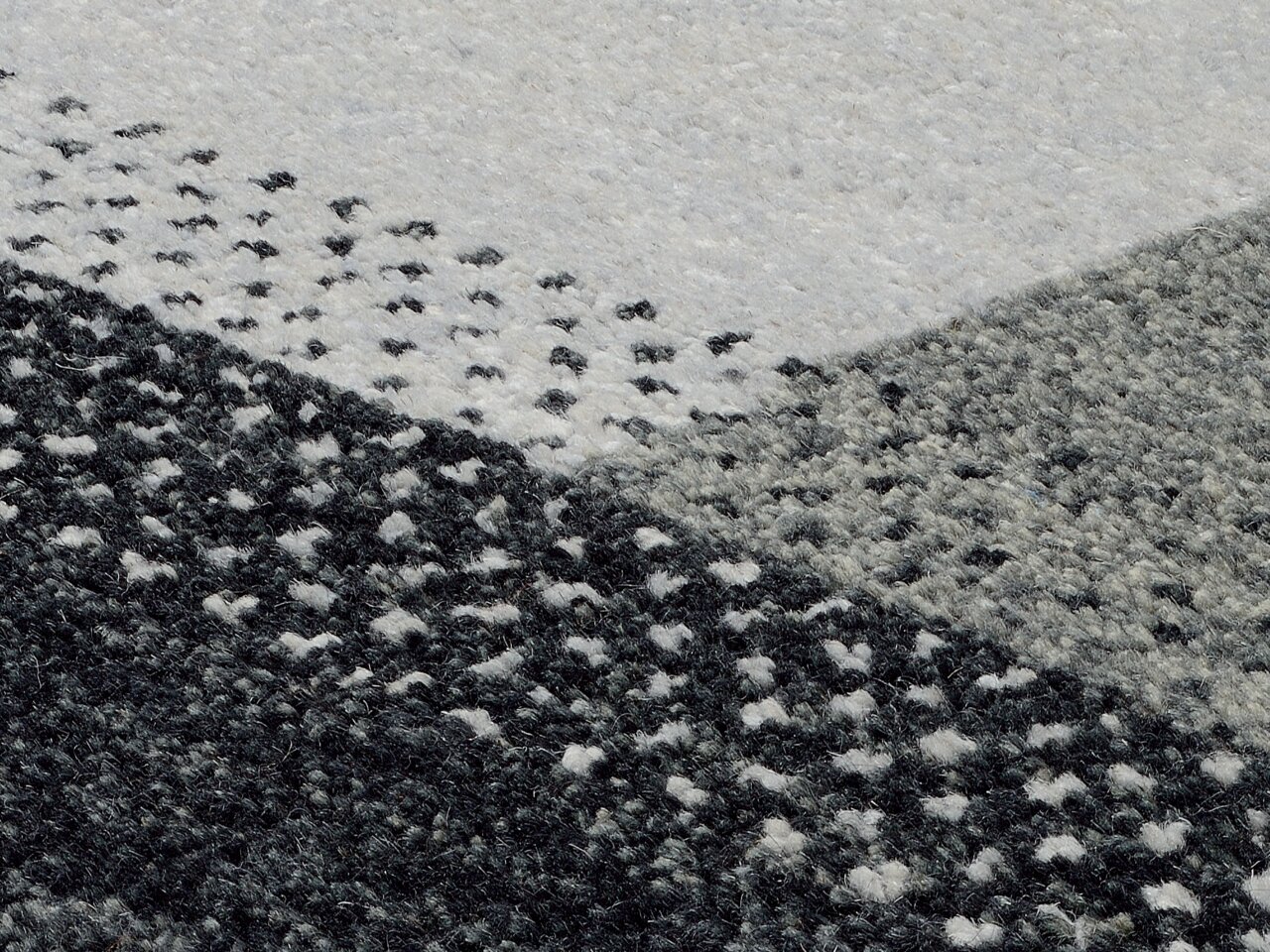 Nahaufnahme eines Wollteppichs mit geometrischem Muster in Grautönen, von oben betrachtet.