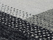 Nahaufnahme eines Wollteppichs mit geometrischem Muster in Grautönen, von oben betrachtet.