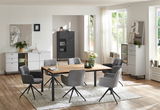 Moderner Esstisch mit Holzplatte und schwarzen Metallbeinen, umgeben von grauen Polsterstühlen in einem hellen Wohnzimmer mit großen Fenstern, aus der Perspektive des Raumes betrachtet.