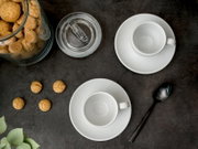 Draufsicht auf zwei weiße Kaffeetassen mit Untertassen neben einem Glas mit Keksen, einer Zuckerdose und einem schwarzen Löffel auf dunkler Oberfläche