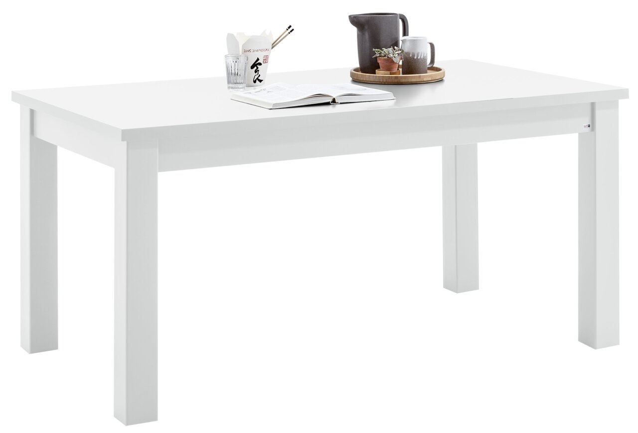 Set one by Musterring Esstisch TACOMA Weißer Esstisch aus der Serie Set one by Musterring, Modell TACOMA, mit Dekorationen wie einem Buch, einer Tasse und einer kleinen Pflanze, aus seitlicher Perspektive fotografiert.