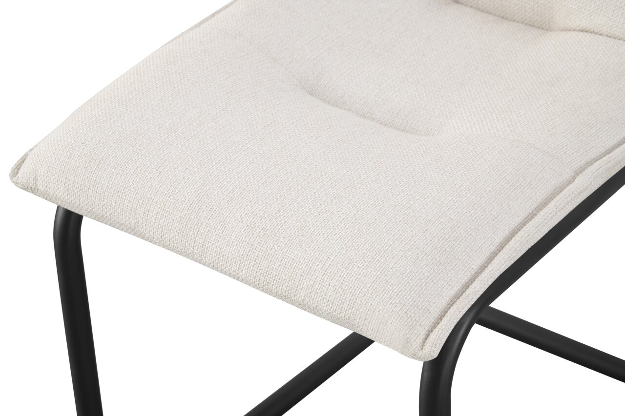 Nahaufnahme eines gepolsterten Sitzkissens in hellem Beige auf schwarzem Metallgestell, schräg von oben fotografiert