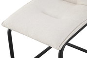 Nahaufnahme eines gepolsterten Sitzkissens in hellem Beige auf schwarzem Metallgestell, schräg von oben fotografiert
