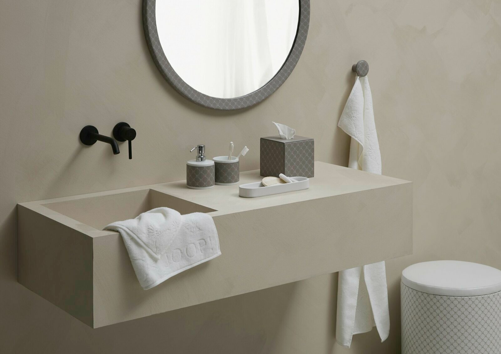 Moderner Badezimmer-Waschtisch mit rundem Spiegel, schwarzem Wasserhahn und Porzellan-Seifenspender in Weiß mit grauem Muster, seitliche Perspektive.