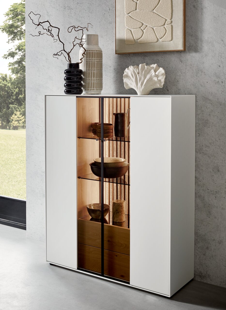Modernes Highboard mit weißer Front und Glastüren, dekoriert mit Vasen und Kunstobjekten, seitliche Perspektive