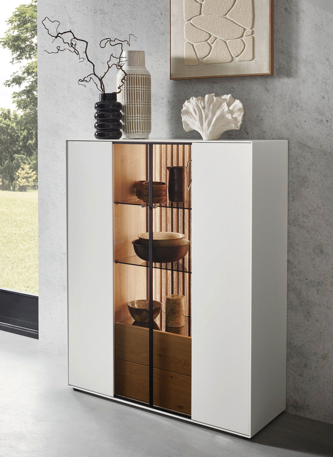 Modernes Highboard mit weißer Front und Glastüren, dekoriert mit Vasen und Kunstobjekten, seitliche Perspektive