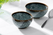 Zwei blaue Dessertschalen aus Keramik mit glänzender Oberfläche, von schräg oben fotografiert, neben einem Löffel auf einem weißen Tisch.