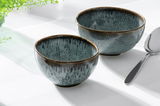 Zwei blaue Dessertschalen aus Keramik mit glänzender Oberfläche, von schräg oben fotografiert, neben einem Löffel auf einem weißen Tisch.
