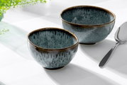 Zwei blaue Dessertschalen aus Keramik mit glänzender Oberfläche, von schräg oben fotografiert, neben einem Löffel auf einem weißen Tisch.