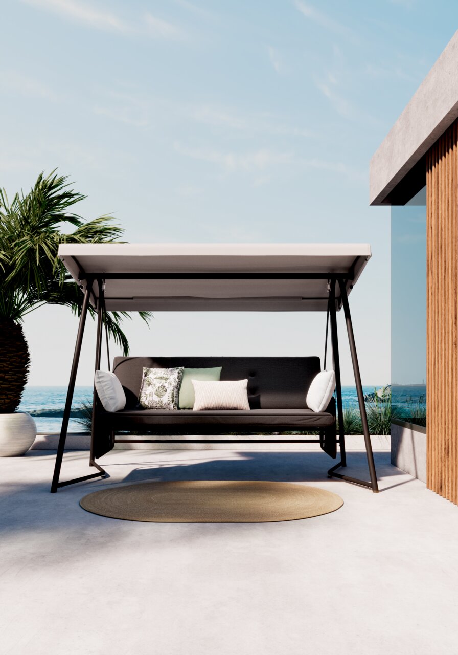 Moderne Hollywoodschommel met een zwart frame en een grijze kap, omringd door kussens, op een terras met uitzicht op zee, gezien vanuit de voorkant.