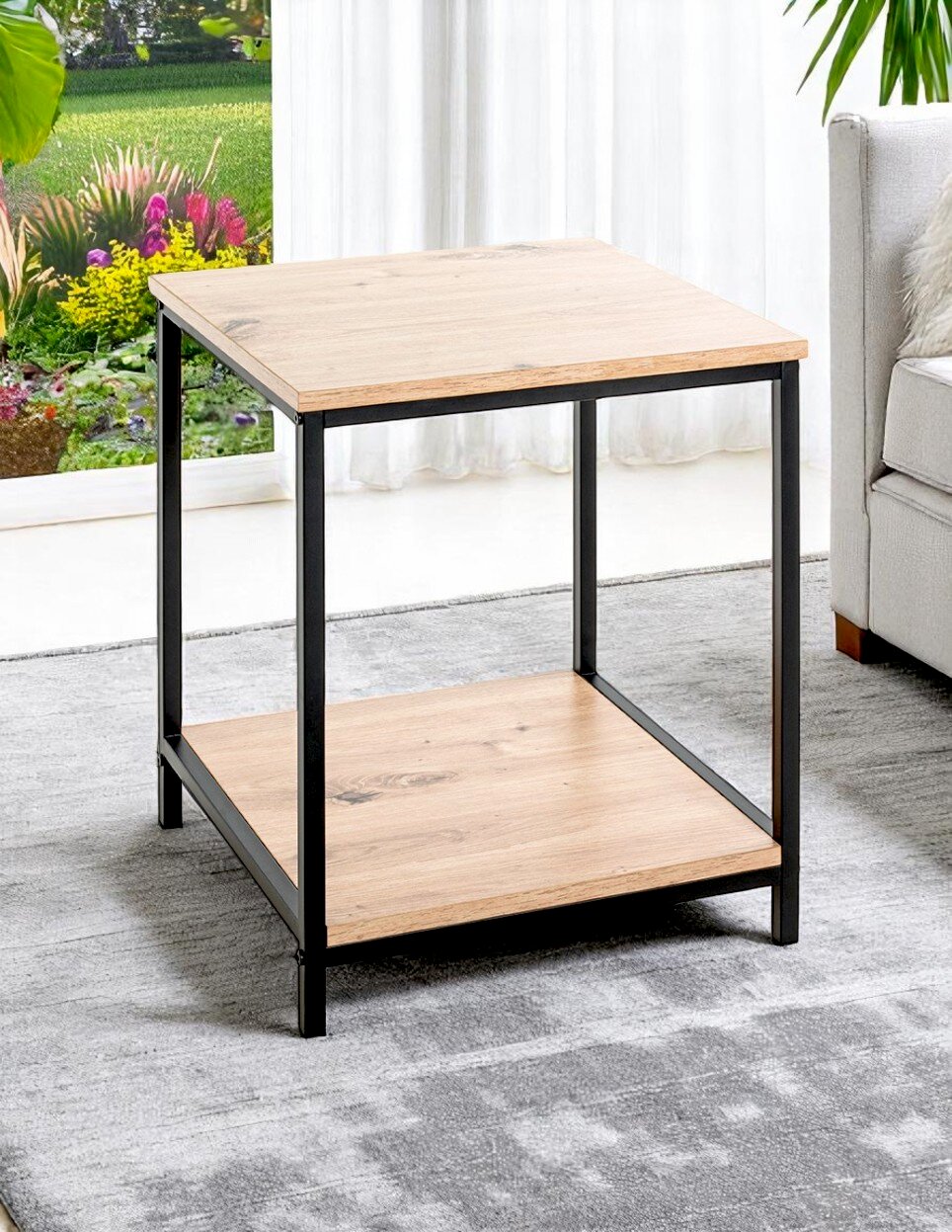 Quadratischer Beistelltisch im Industrial-Design mit heller Holzoptik und schwarzem Metallrahmen sowie Ablageboden, fotografiert in schräger Vorderansicht im Wohnzimmer neben einem Sofa.