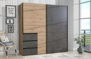 Moderner Schwebetürenschrank WINN2 in Holz- und Betonoptik, seitliche Perspektive, in einem hellen Raum mit Dekoration.