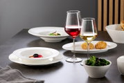 Elegante Speiseteller und Schalen in einem modernen Tischarrangement mit Rot- und Weißweingläsern, seitliche Perspektive.