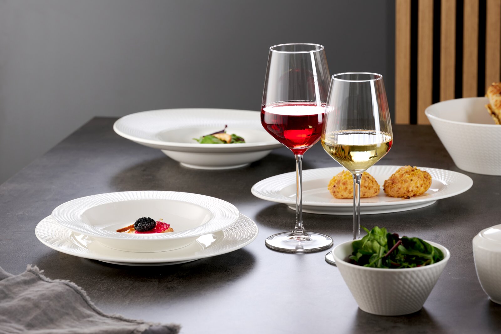 Elegante Speiseteller und Schalen in einem modernen Tischarrangement mit Rot- und Weißweingläsern, seitliche Perspektive.
