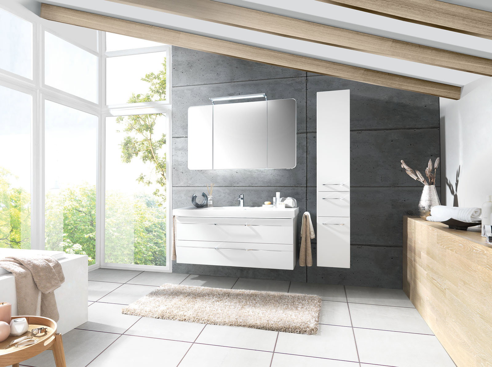 Moderne Badkombination mit weißem Waschtisch und Spiegelschrank, seitlich von einem hohen Schrank flankiert, in einem hellen Badezimmer mit großen Fenstern und Holzbalkendecke, Perspektive von vorne.