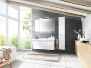 Moderne Badkombination mit weißem Waschtisch und Spiegelschrank, seitlich von einem hohen Schrank flankiert, in einem hellen Badezimmer mit großen Fenstern und Holzbalkendecke, Perspektive von vorne.