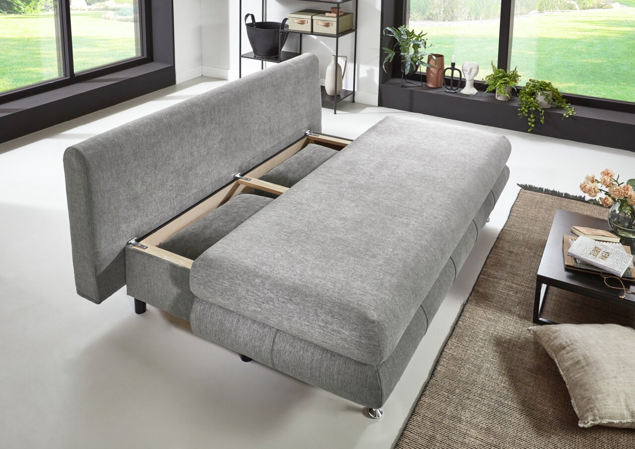 Graues Funktionssofa in moderner Wohnzimmereinrichtung, von schräg oben fotografiert, mit ausgezogenem Bettmechanismus.
