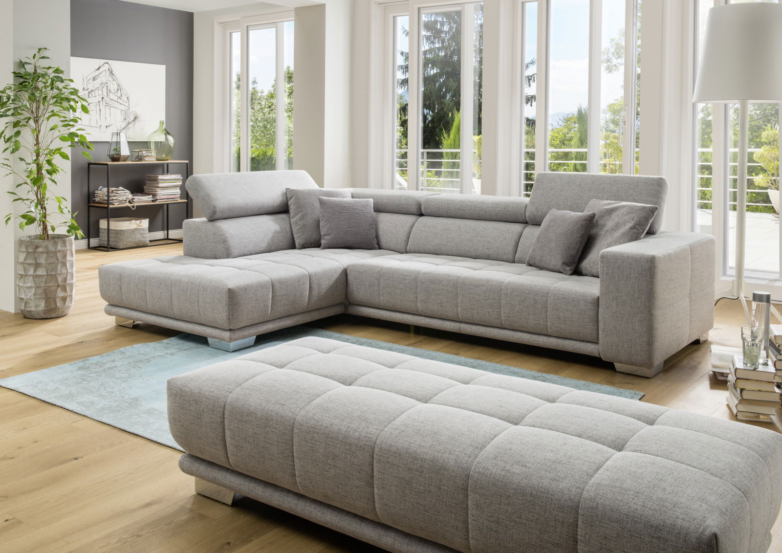 Moderne graue Polsterrundecke in einem hellen Wohnzimmer mit großen Fenstern, seitliche Perspektive