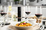 Zwei elektrische Pfeffer- und Salzmühlen in Schwarz und Weiß auf einem gedeckten Tisch mit Weingläsern und einem Teller Pasta, aus der Perspektive von vorne.