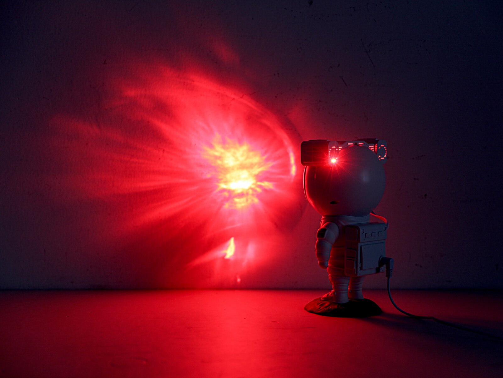 LED-Dekoleuchte in Form eines Astronauten, der einen roten Lichtstrahl an die Wand projiziert. Perspektive von hinten rechts.