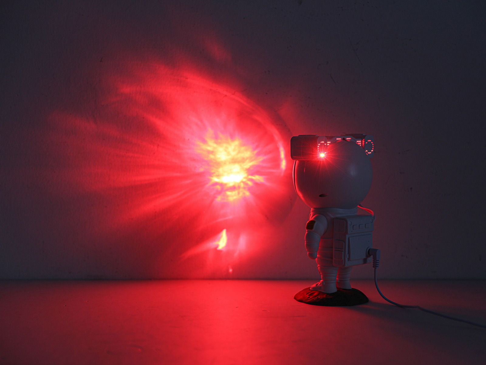 LED-Dekoleuchte in Form eines Astronauten, der einen roten Lichtstrahl an die Wand projiziert. Perspektive von hinten rechts.