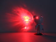 LED-Dekoleuchte in Form eines Astronauten, der einen roten Lichtstrahl an die Wand projiziert. Perspektive von hinten rechts.