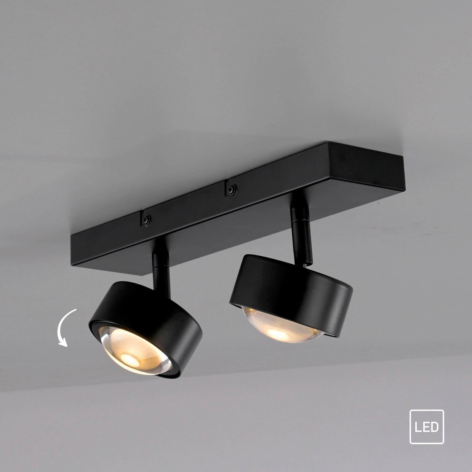 Schwarzer LED-Deckenstrahler mit zwei schwenkbaren Spotköpfen an rechteckiger Deckenhalterung, warmweiß leuchtend, Ansicht schräg von unten