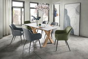 Moderner Esstisch mit weißer Tischplatte und Holzbeinen, umgeben von gepolsterten Stühlen in Grau und Grün, in einem hellen Raum mit großen Fenstern, aus seitlicher Perspektive.