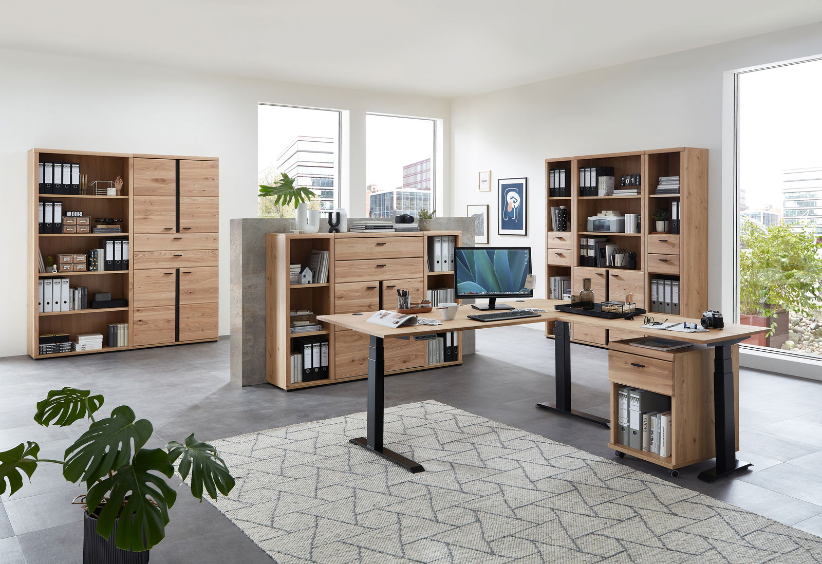 Moderne Büromöbel in einem hellen Raum mit großen Fenstern, bestehend aus einem Eckschreibtisch, mehreren Aktenschränken und Regalen aus Holz. Perspektive von vorne.