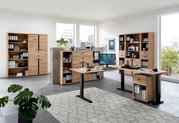 Moderne Büromöbel in einem hellen Raum mit großen Fenstern, bestehend aus einem Eckschreibtisch, mehreren Aktenschränken und Regalen aus Holz. Perspektive von vorne.