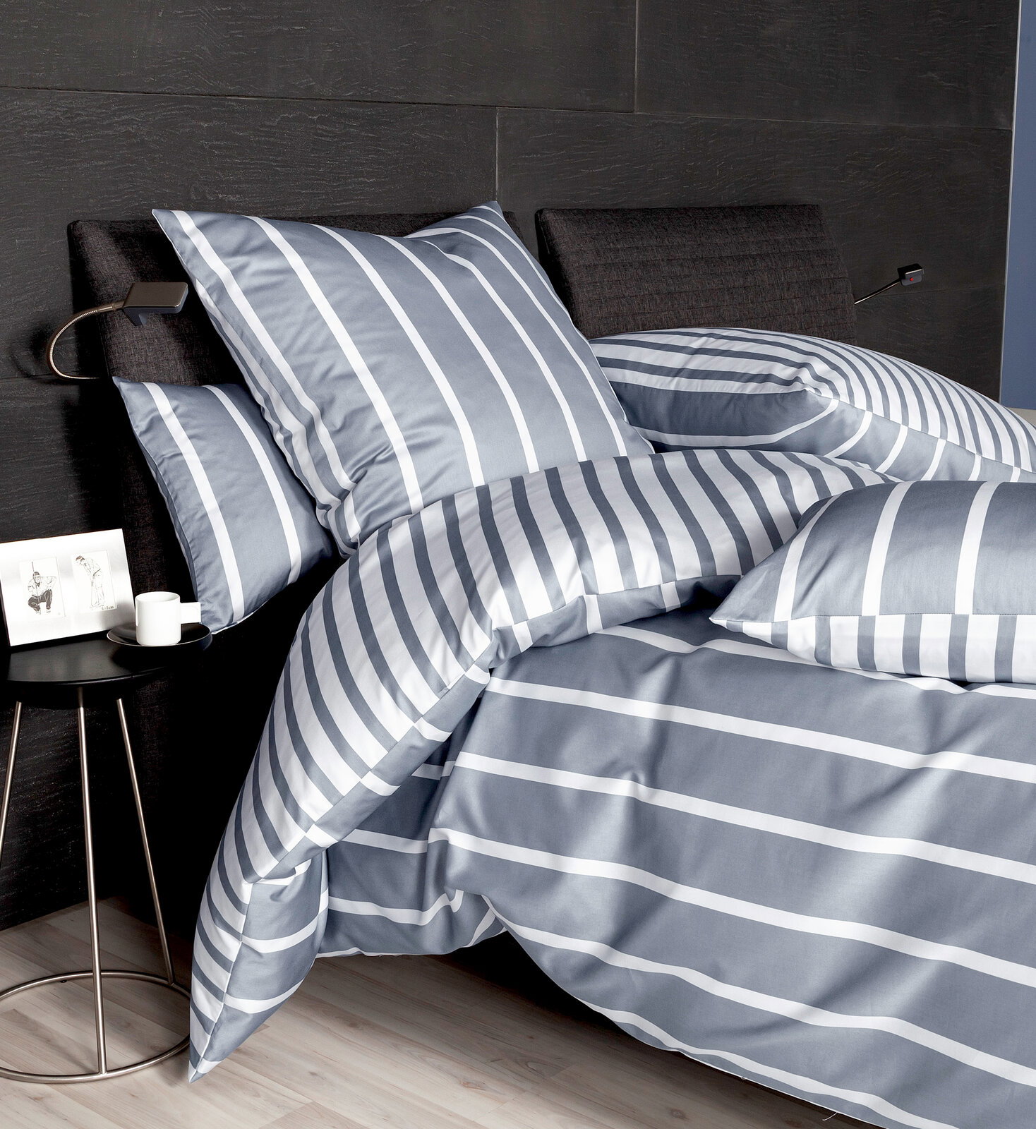 Bettwäsche-Set in Grau mit weißen Streifen, auf einem Bett mit dunklem Kopfteil, seitliche Perspektive