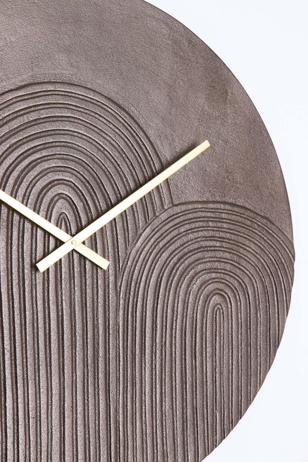 Nahaufnahme einer modernen Wanduhr mit strukturiertem, kreisförmigem Muster und goldenen Zeigern.