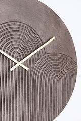 Nahaufnahme einer modernen Wanduhr mit strukturiertem, kreisförmigem Muster und goldenen Zeigern.