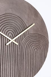 Nahaufnahme einer modernen Wanduhr mit strukturiertem, kreisförmigem Muster und goldenen Zeigern.