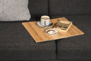 Bambus Sofaablage auf einem grauen Sofa mit einer Tasse Kaffee, einem Buch und einer Schale mit Süßigkeiten, aus der Vogelperspektive.