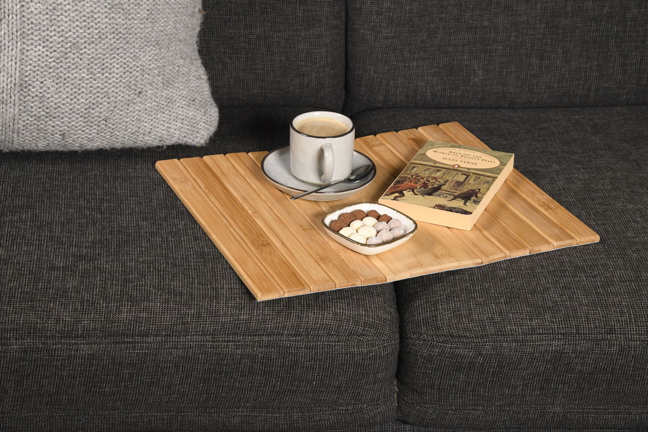 Bambus Sofaablage auf einem grauen Sofa mit einer Tasse Kaffee, einem Buch und einer Schale mit Süßigkeiten, aus der Vogelperspektive.