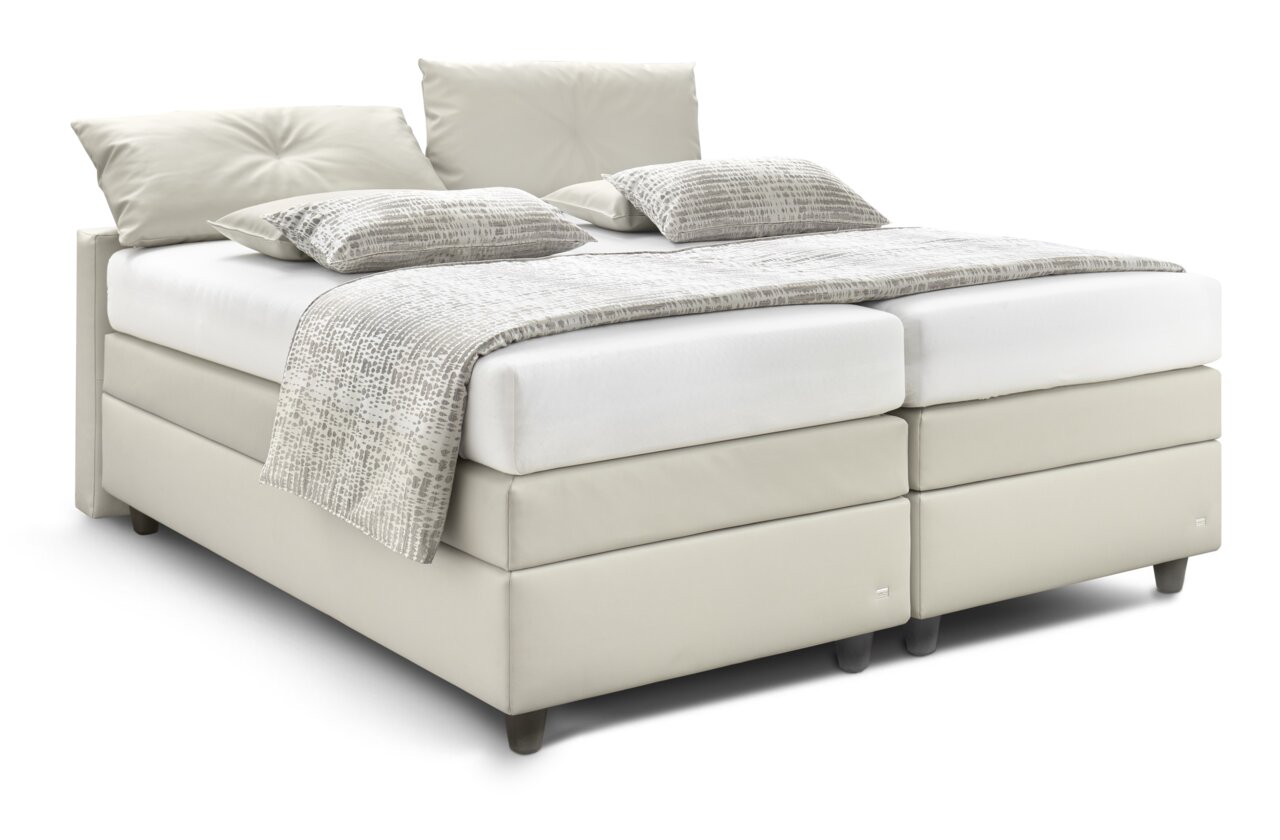 Boxspringbed QLX BKA in lichtbeige, zijaanzicht, met twee kussens en een gedessineerde deken.