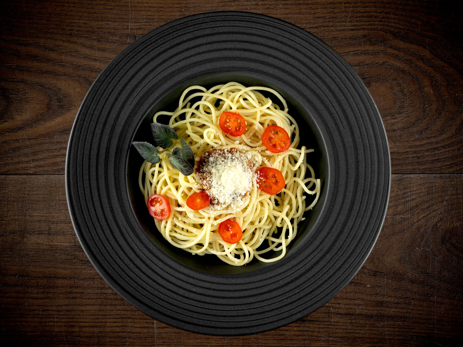 Creatable Pastateller 2-tlg LAVA STONE Draufsicht auf einen schwarzen Teller mit Spaghetti, geriebenem Käse, Kirschtomatenscheiben und Kräutern auf einem Holztisch
