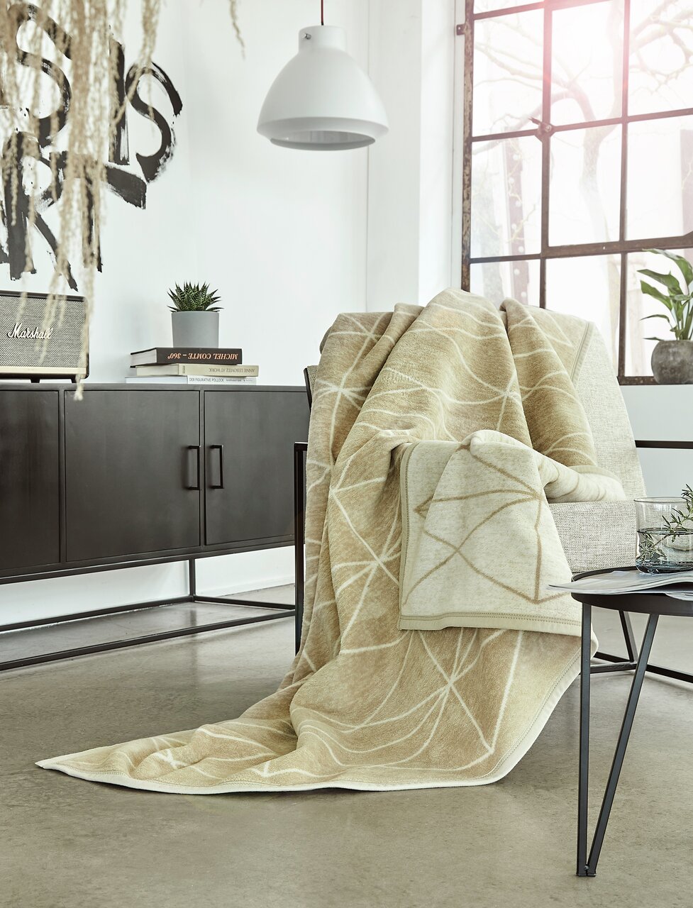 IBENA Decke 150x200cm BUGATTI EX Beige Jacquard-Decke 150x200 cm auf einem Sessel in einem modernen Wohnzimmer, seitliche Perspektive