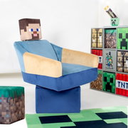 Op Minecraft geïnspireerde kinderfauteuil in blauw en beige met een kussen met pixelprint, schuin van linksvoor gefotografeerd, naast een plank met Minecraft-motieven op een witte achtergrond