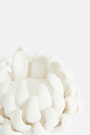 Nahaufnahme eines weißen Teelichthalters mit strukturierter Oberfläche und blütenblattartigem Design, von oben betrachtet.