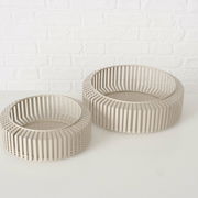 Zwei moderne, runde Schalen aus beigem Material mit einem Gitterdesign, auf einer weißen Oberfläche vor einer weißen Ziegelwand, aus einer leicht erhöhten Perspektive fotografiert.