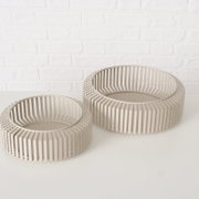 Zwei moderne, runde Schalen aus beigem Material mit einem Gitterdesign, auf einer weißen Oberfläche vor einer weißen Ziegelwand, aus einer leicht erhöhten Perspektive fotografiert.