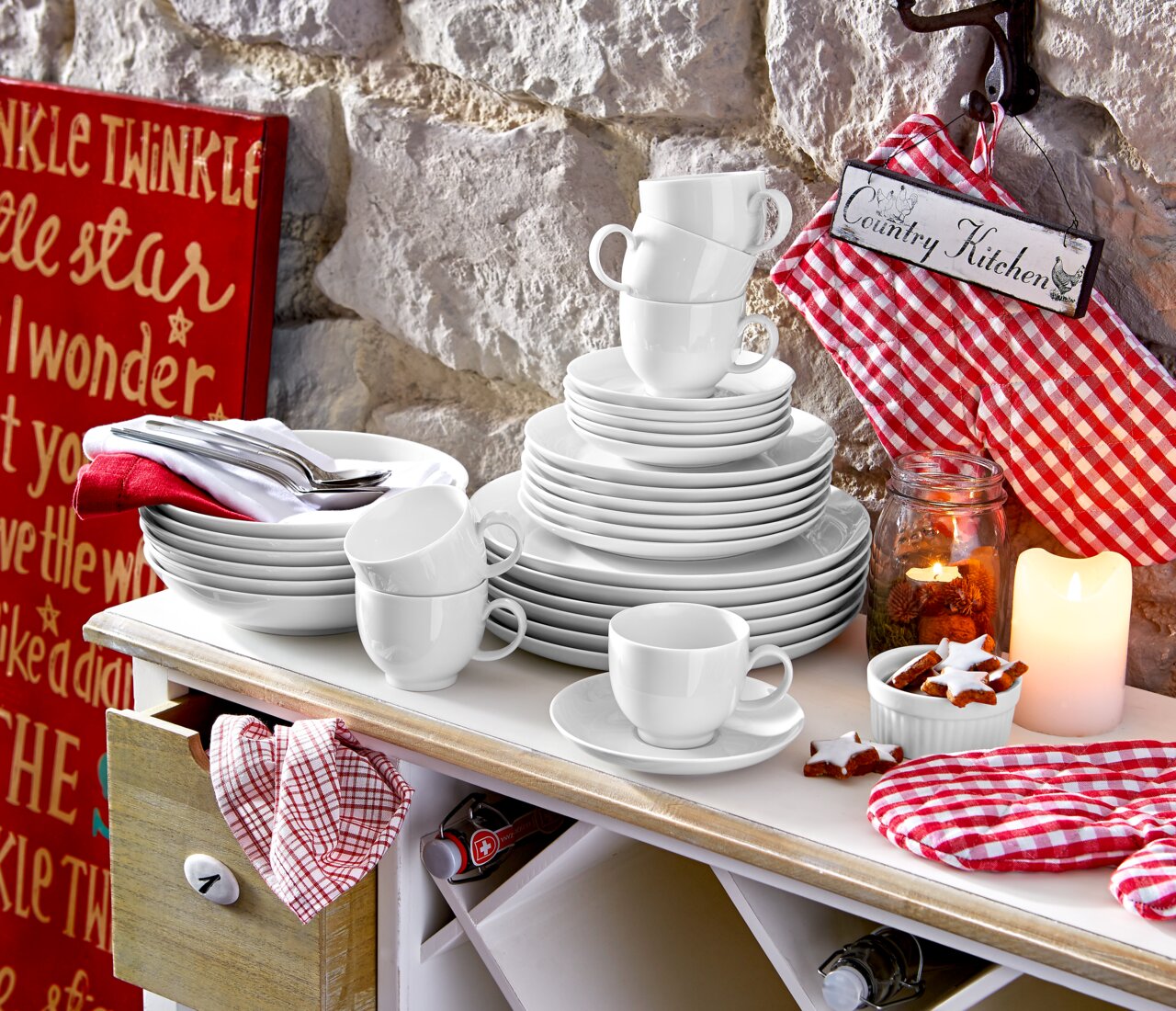 Ein stilvolles weißes Kombiservice-Set, bestehend aus Tellern, Tassen und Schalen, auf einem Tisch in einer gemütlichen Landhausküche. Perspektive von vorne.