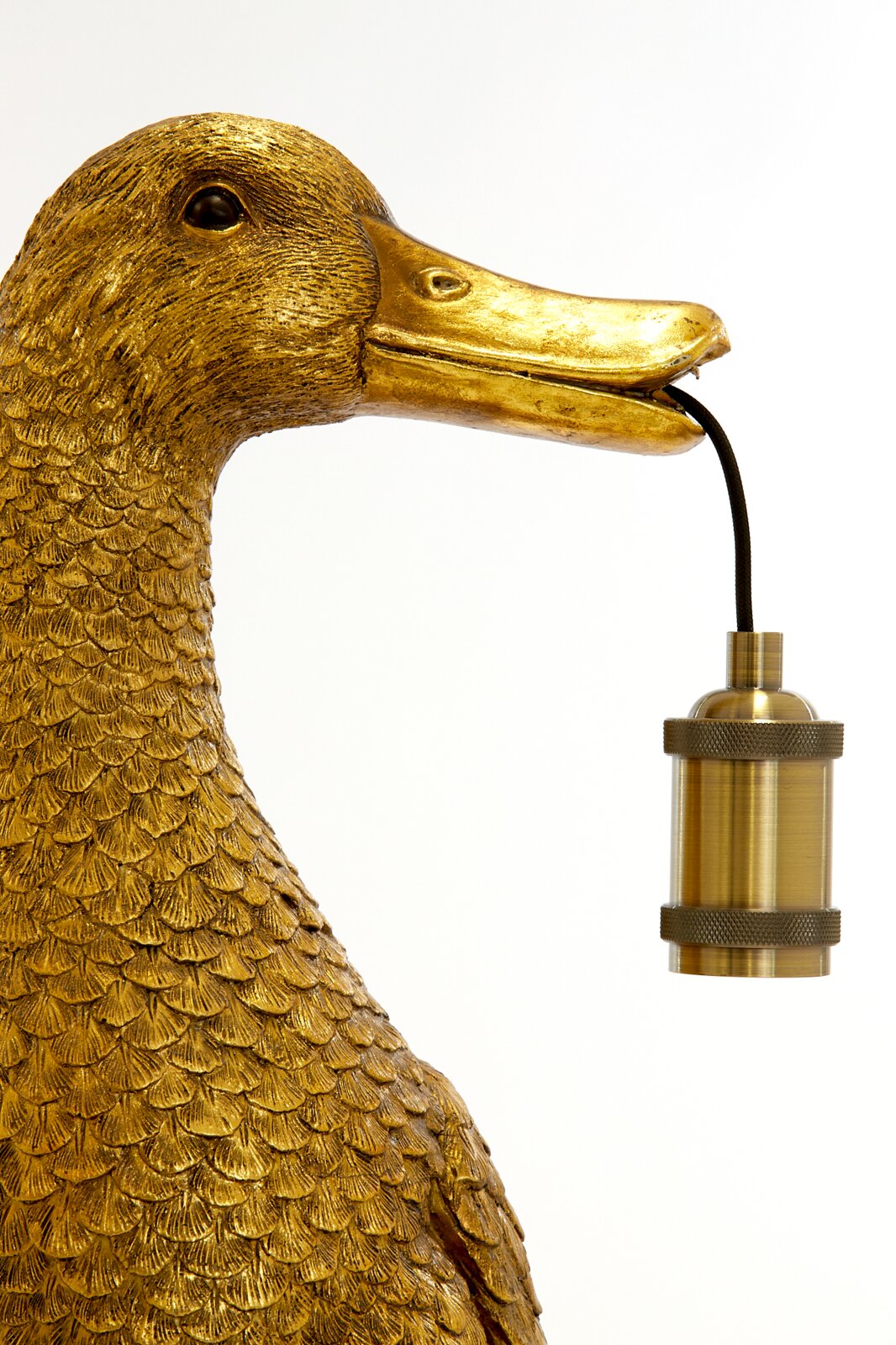 Close-up van een gouden tafellamp in de vorm van een eend, die een lampvoet in zijn snavel houdt.