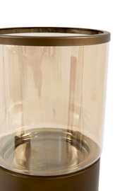 Detailopname vanuit een licht verhoogd vooraanzicht van een elegant cilindervormig windlicht in amberkleurig glas met bronskleurige metalen rand en voet.