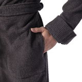 Nahaufnahme eines grauen Kapuzenbademantels in Größe M, mit einer Hand in der Tasche und einem Gürtel um die Taille, seitliche Perspektive.