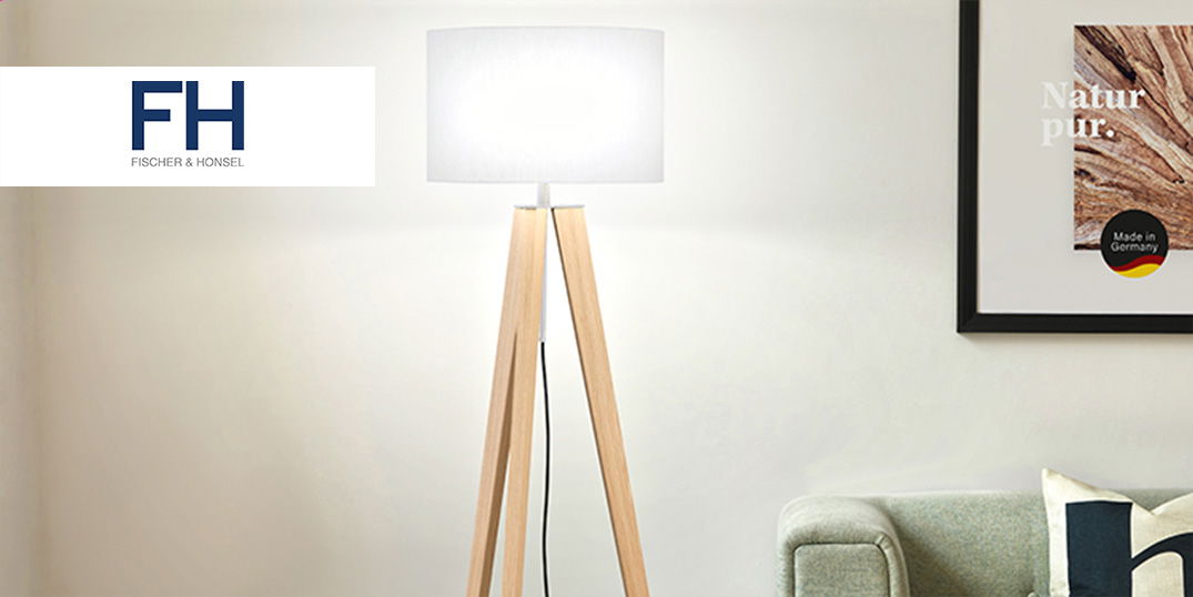 Eine moderne Stehlampe mit Holzfüßen leuchtet neben einem Sofa in einem hellen Wohnzimmer.