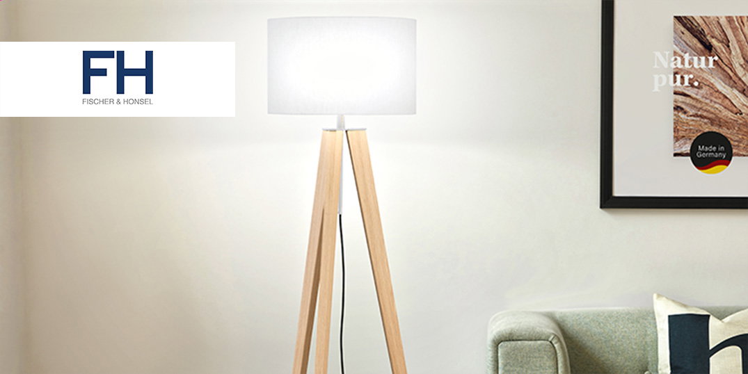 Een moderne staande lamp met houten poten staat naast een bank in een lichte woonkamer.